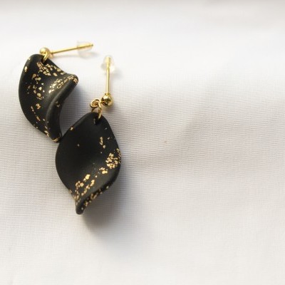 Brincos pretos com padrões dourados sobre tecido branco