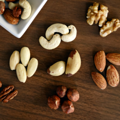 Vários frutos secos crus sobre uma mesa de madeira escura, incluindo amêndoas, avelãs e nozes