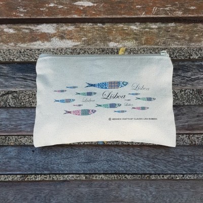 Bolsa de tecido bege claro com ilustração de peixes coloridos e texto Lisboa, sobre banco de madeira