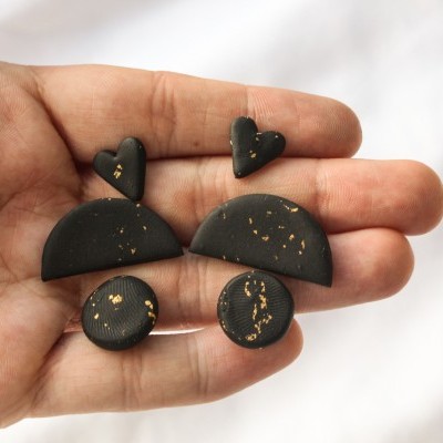 Brincos pretos com manchas douradas exibidos em mão contra fundo branco