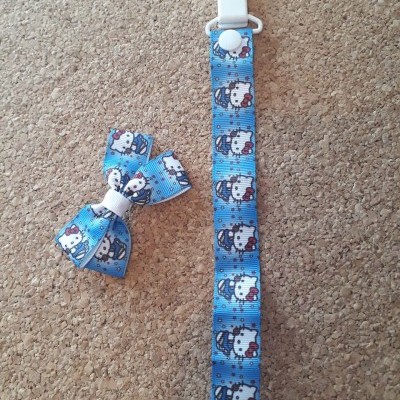 Prendedor para chupeta e laço azul com padrão Hello Kitty sobre fundo de cortiça