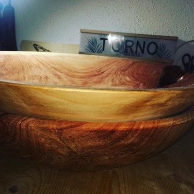 Taças de madeira empilhadas sobre mesa de madeira com placa 'TORNO' ao fundo.