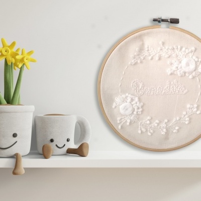 Vasos cinzentos sorridentes com flores amarelas e bastidor de costura com bordado branco numa prateleira branca