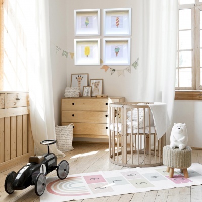 Quarto de bebé com berço de madeira, cómoda, tapete colorido, carrinho preto e quadros de gelados