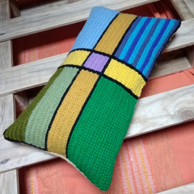 almofada retangular colorida em croché sobre estrutura de madeira clara e tecido laranja listrado