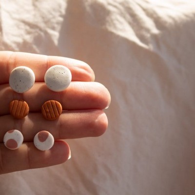 Brincos pequenos redondos em três estilos e cores diferentes na mão contra fundo de tecido claro