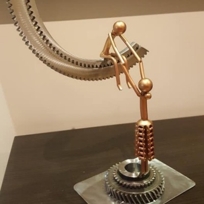 Escultura metálica decorativa com figuras humanas e peças de engrenagem em tons metálicos