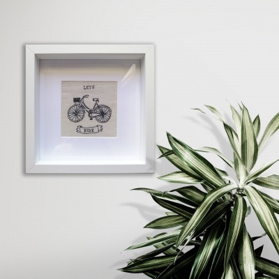 Quadro branco com imagem de bicicleta e texto LET'S RIDE ao lado de planta verde