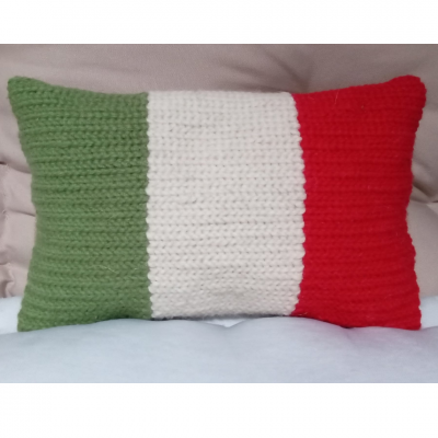 Almofada tricotada verde, branca e vermelha sobre superfície clara