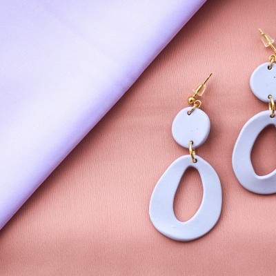 Brincos lilás em forma oval e circular sobre tecido rosa e lilás