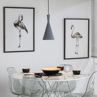 Sala de jantar com mesa branca e cadeiras transparentes, luminária cinza e quadros de flamingos.
