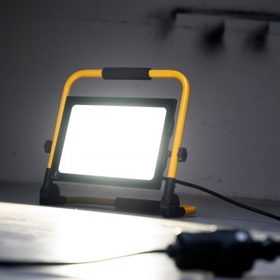 Projetor LED portátil amarelo e preto ligado e a iluminar em chão interior