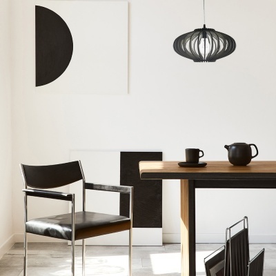 Interior minimalista com cadeira preta, mesa de madeira, jarra e caneca pretas, pinturas modernas e candeeiro preto.