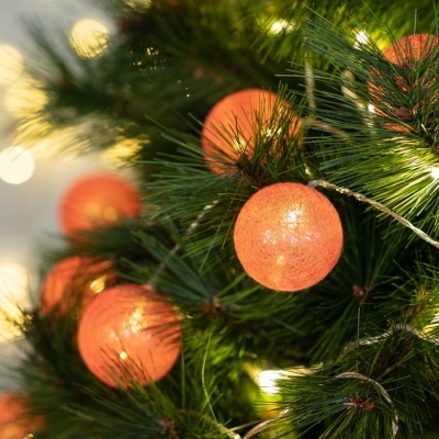 Bolas de Natal laranja brilhantes numa árvore verde com luzes brancas