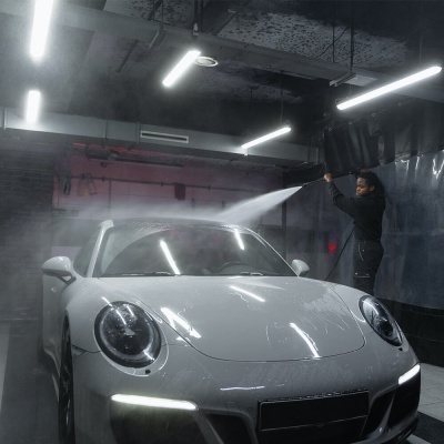 Carro desportivo branco a ser lavado num espaço interior com iluminação fluorescente.