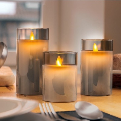 Três velas artificiais em vidro cinza fosco com chama LED amarela na mesa