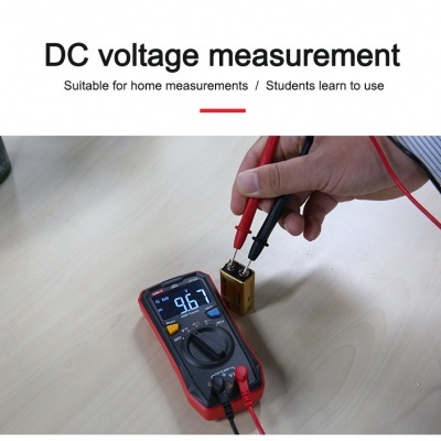 Multímetro digital a medir voltagem de pilha retangular dourada sobre mesa clara