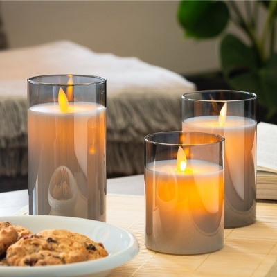 Três velas em copos de vidro cinza acesas sobre mesa com bolachas e livro ao fundo