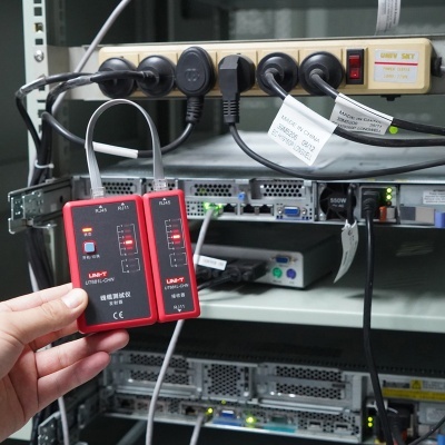 Dispositivo de teste de cabos LAN vermelho e preto segurado à frente de servidores e régua de tomadas