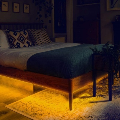 Cama de madeira com colcha azul turquesa e almofadas decorativas em quarto com iluminação LED