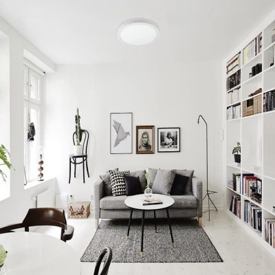 Sala de estar moderna com sofá cinzento, mesas de centro redondas brancas, estante branca com livros e decoração com quadros na parede