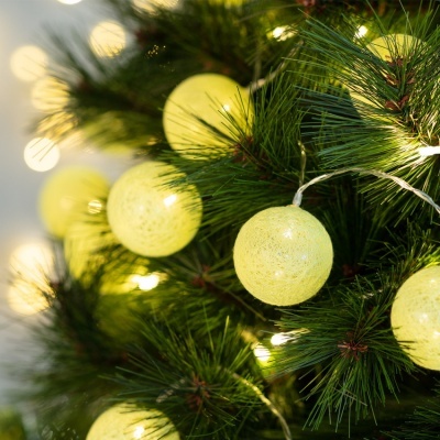 Bolas luminosas amarelas de Natal em ramo de pinheiro verde