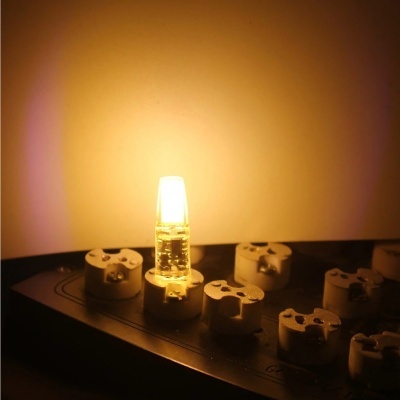 Lâmpada LED amarela quente ligada em base preta com suportes brancos num ambiente escuro