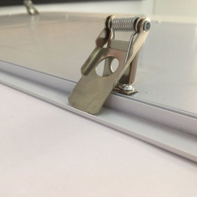 Clipe metálico prateado com mola fixado numa base metálica cinzenta