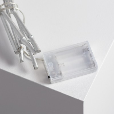 Corda de luzes com fios prateados e caixa de pilhas transparente numa superfície branca