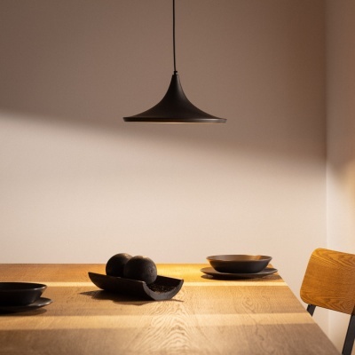 Candeeiro pendente preto acima de mesa de madeira com utensílios pretos e cadeira ao lado