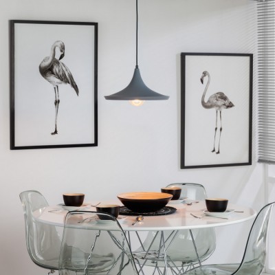 Mesa de jantar redonda com tigelas e cadeiras transparentes, parede branca com quadros de flamingos