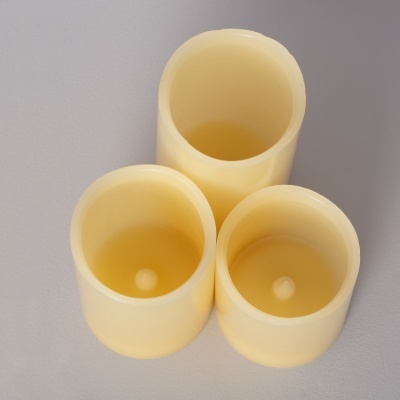 Três velas amarelas artificiais de vários tamanhos sobre superfície cinza