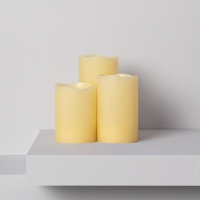 Três velas elétricas creme sobre superfície branca minimalista