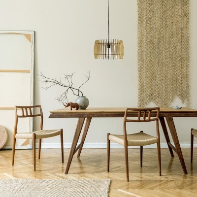 Sala de jantar com mesa e cadeiras de madeira clara, vaso com ramo seco, lâmpada pendente e tapete bege