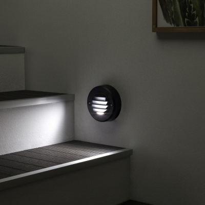 Luz de parede LED redonda preta junto a escadas brancas e piso escuro