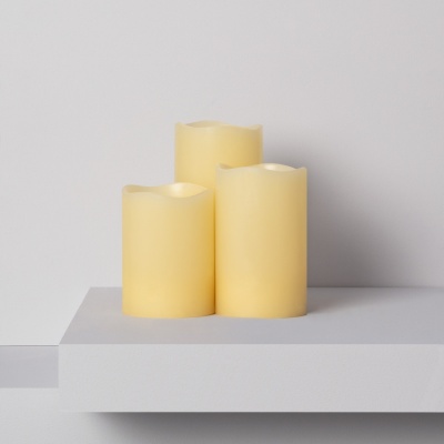 Três velas elétricas creme sobre superfície branca minimalista