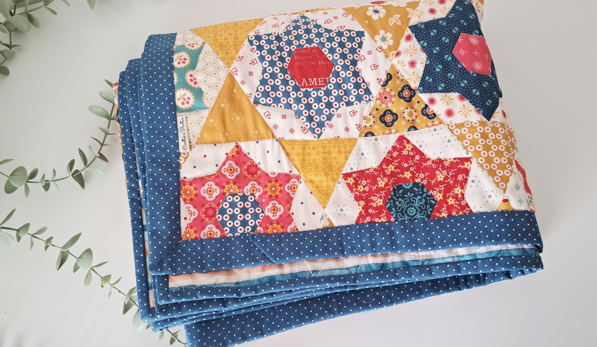 Manta Fake Patchwork Colcha dobrada com padrão de estrelas coloridas e borda azul de pontos brancos