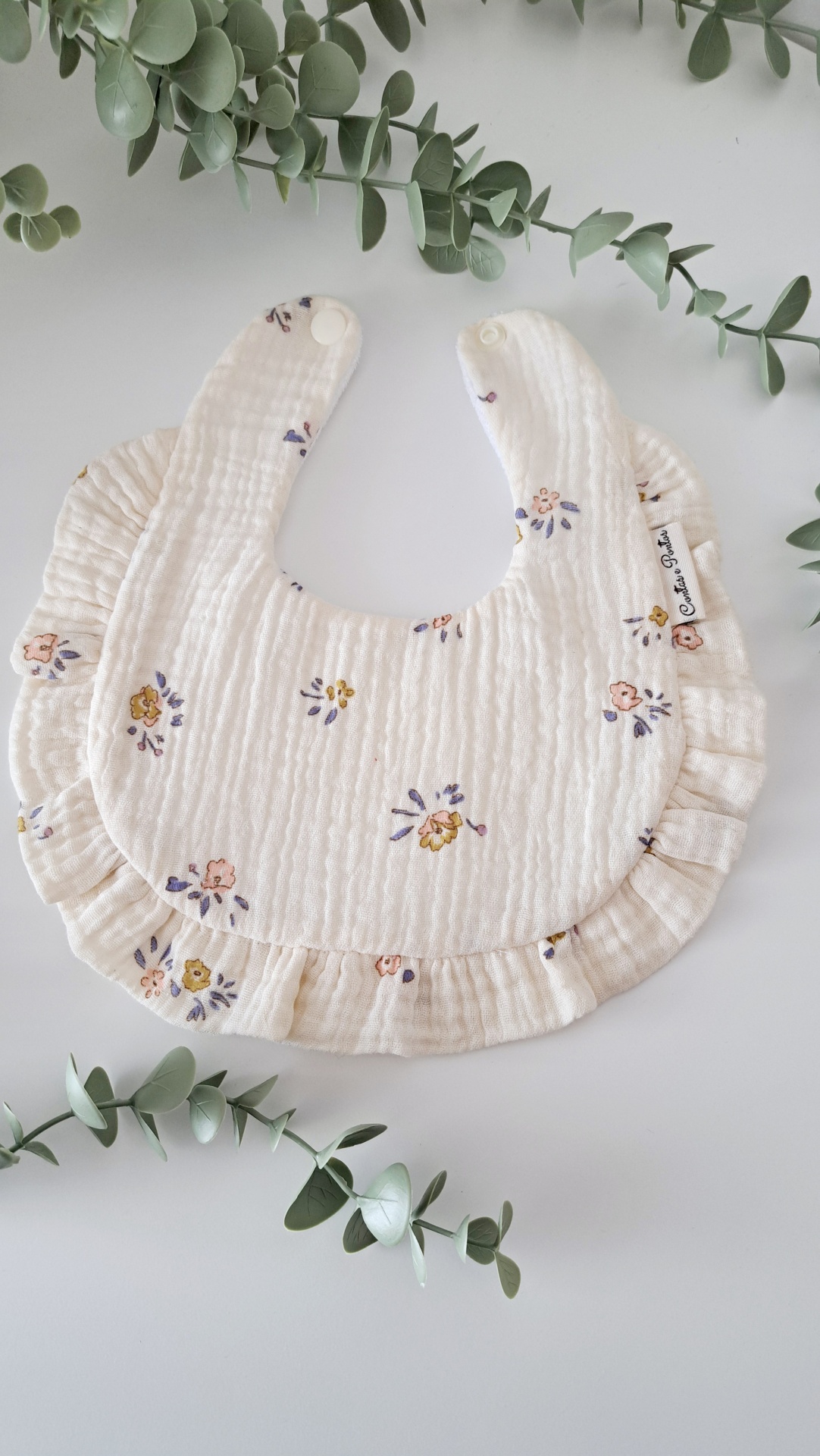 Babete - Floral bouquet Babete branco com flores pequenas e folhos, rodeado por ramos verdes