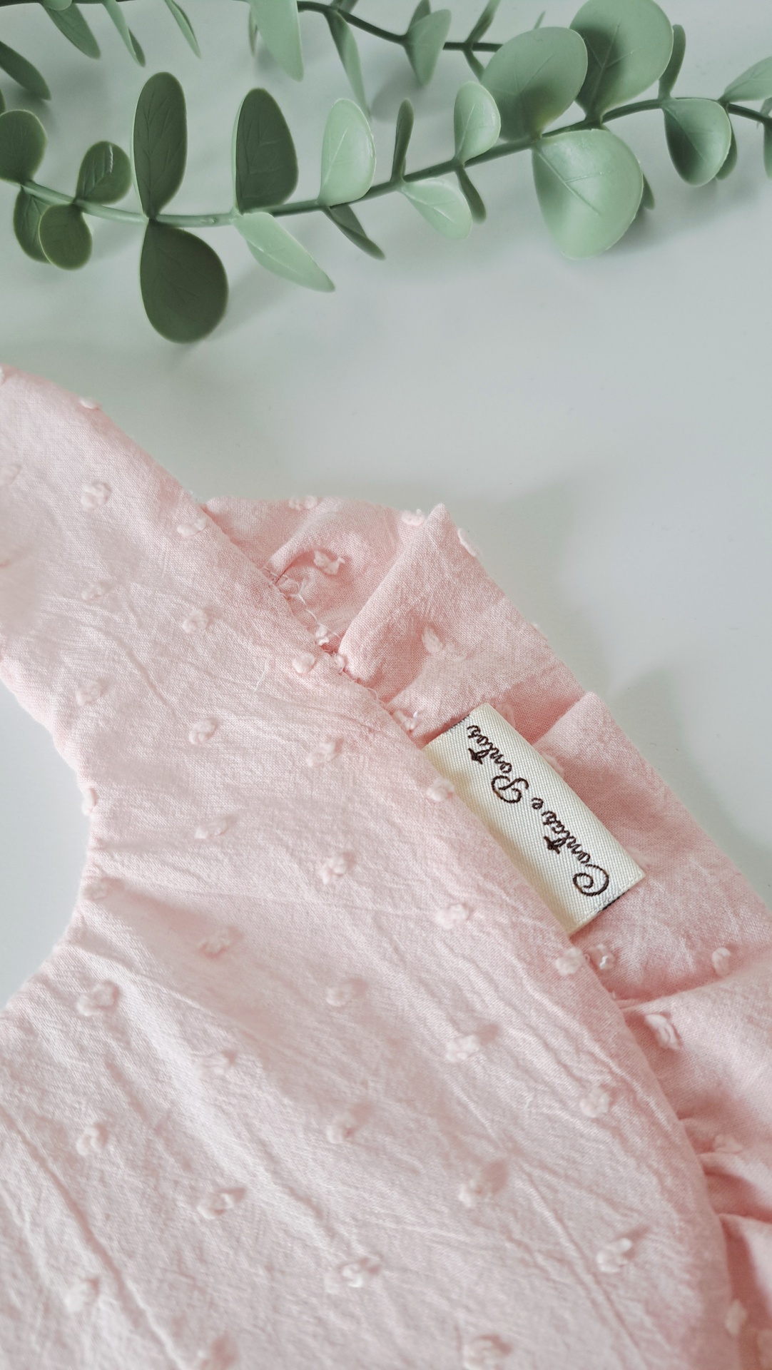 Babete ♥ pale rose Tecido rosa claro com nós em relevo e etiqueta Confete & Pastel perto de ramo verde