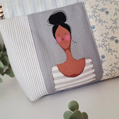 Necessaire de tecido com ilustração de mulher e padrões listrados e florais.