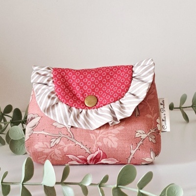 Bolsa pequena de tecido floral rosa com aba vermelha e folho branco, botão dourado e etiqueta Costura e Pontos