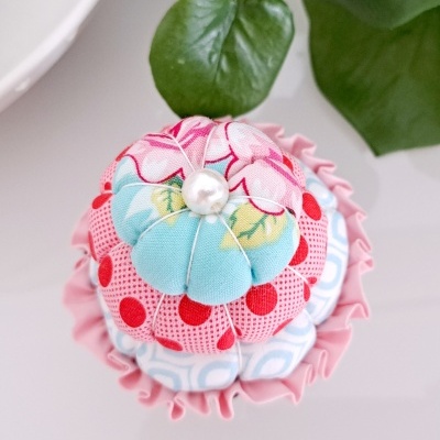 Alfineteiro de tecido colorido com pérola no centro e folha verde ao fundo