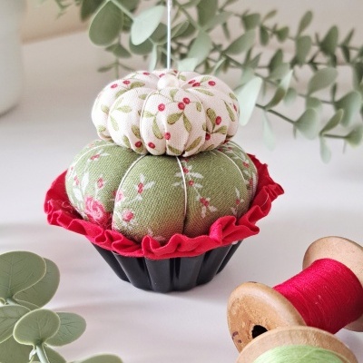 Alfineteiro em tecido floral com carretéis de linha e folhas decorativas