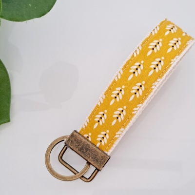 Chaveiro ou pulseira em tecido amarelo com padrão branco e preto, fecho metálico dourado