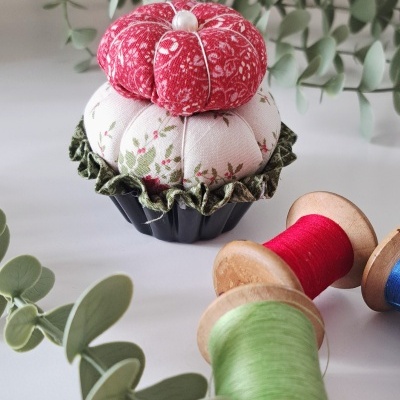 Alfineteiro de tecido em forma de cupcake com carretéis de linha coloridos e plantas ao fundo