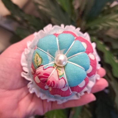 Alfineteira de tecido colorido com botão pérola no centro e renda branca