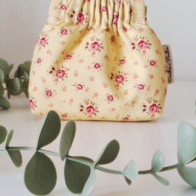 Necessaire de tecido amarelo claro com flores rosas e fecho elástico.