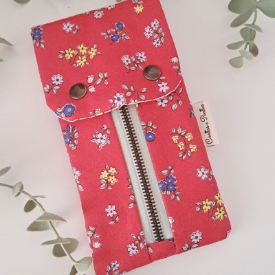 Bolsa ou estojo vermelho com flores e fechos, sobre fundo branco com folhas verdes