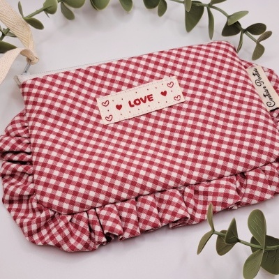 Bolsa ou nécessaire de tecido quadriculado vermelho e branco com etiquetas e babados, decorada com folhas verdes