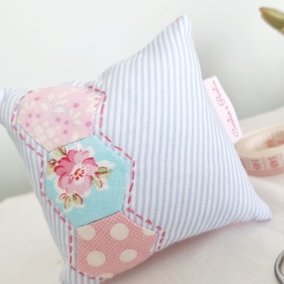 Travesseiro decorativo azul riscado com padrões florais e de bolinhas, perto de fita métrica e planta